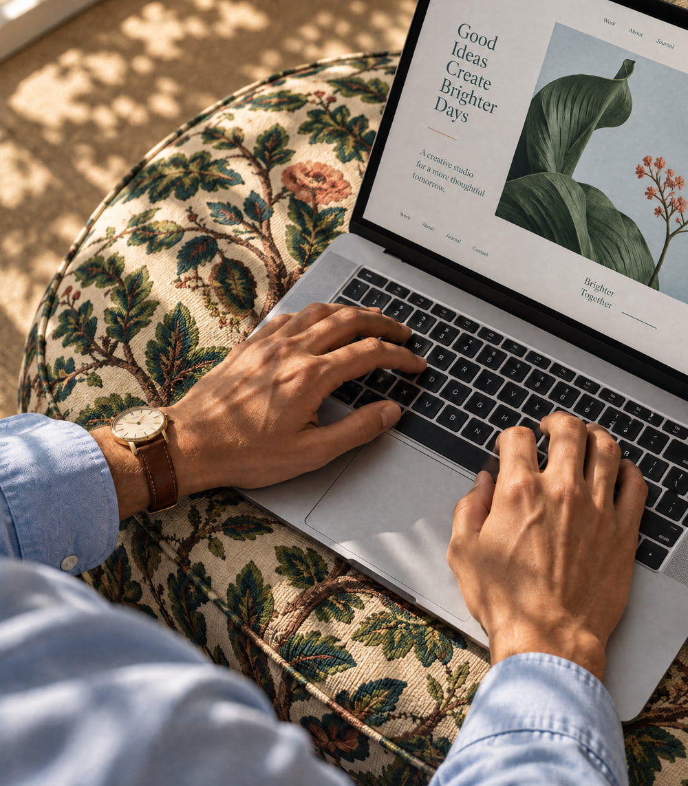 Hands working at a laptop on a patterned ottoman in sunlight